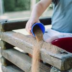 toddler pouring sand in brown wooden fence