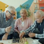 Three seniors playing chess together in a living room.