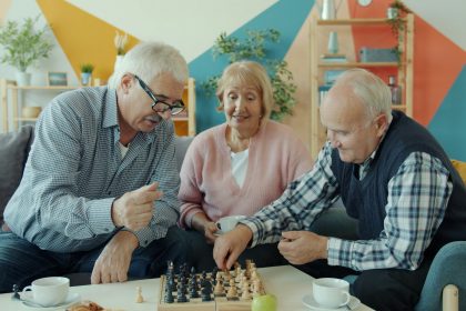 Three seniors playing chess together in a living room.