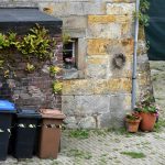 Three trash bins next to a stone building.