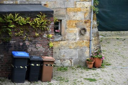 Three trash bins next to a stone building.