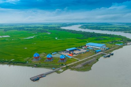 Industrial complex on a riverbank with green fields.