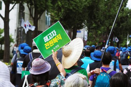 person holding Hangul script sign surrounded by people wearing hats during daytime