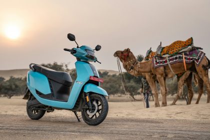 Scooter and camels in the desert at sunset.
