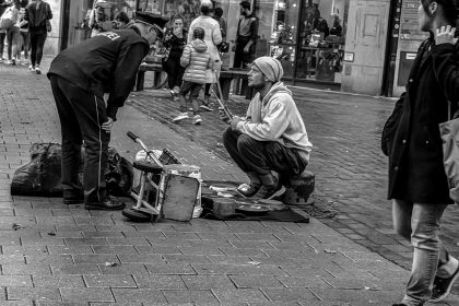 man in black jacket sitting on sidewalk near road