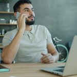 Man talking on phone at desk with laptop.