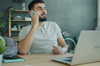 Man talking on phone at desk with laptop.