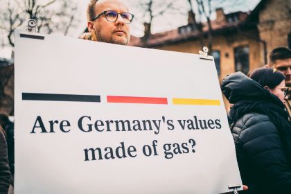 a man holding a sign that says are germany's values made of gas?