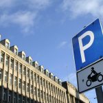 A blue parking sign sitting next to a tall building