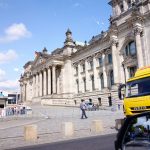 German flag flying near the reichstag building with vehicles.